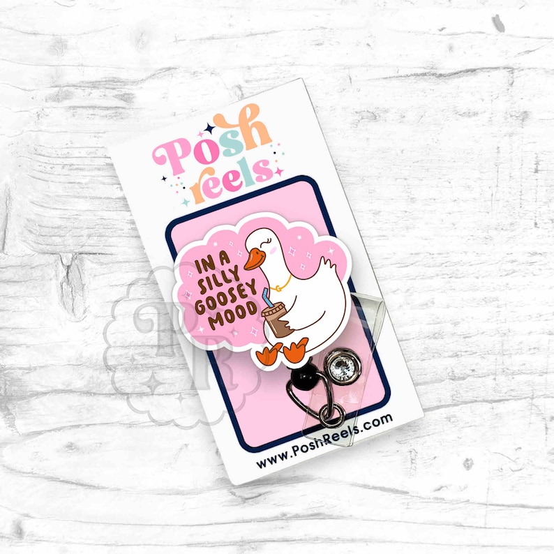 Puede incluir: Una tarjeta rosa y blanca con un ganso de dibujos animados sosteniendo una taza de caf&eacute;. La tarjeta dice "In a silly goosey mood". La tarjeta est&aacute; unida a un portagafete transparente con un carrete retr&aacute;ctil de gafete negro y plateado.