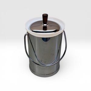 May include: A cylindrical ice bucket with a polished chrome finish, featuring a white plastic rim, a matching chrome swing handle, and a dark brown wooden knob centered on the circular lid. The container has a smooth, reflective surface.