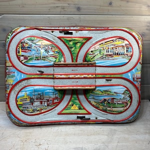 May include: Vintage tin toy race track with a red, white, and blue color scheme. The track features four different scenes, including a city, a lake, a mountain, and a factory. The track is made of metal and has a winding design.