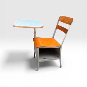 May include: Vintage school desk chair with a light blue writing surface and a wooden seat and back. The chair has a metal frame and a storage shelf underneath. The desk is a classic piece of classroom furniture.