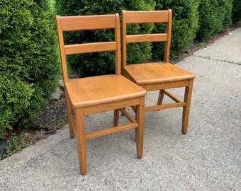 May include: Two wooden chairs with a simple design. The chairs have a light brown finish and are made of solid wood. The chairs are in good condition and would be a great addition to any dining room or kitchen.