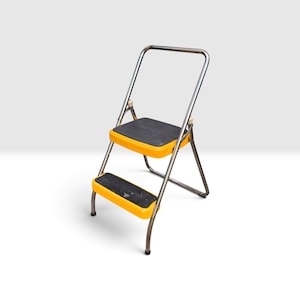 May include: A two-step folding ladder featuring a silver metal frame and bright yellow plastic step housings. Each step has a black, textured, non-slip surface. The ladder includes a tall, U-shaped silver metal handle for stability and support.