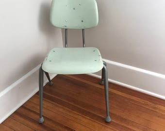 May include: A light green metal chair with a metal frame and four legs. The chair has a simple design and is in good condition.