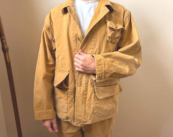 May include: A tan corduroy jacket and matching pants set. The jacket has multiple pockets and a button closure. The outfit is worn over a white t-shirt. The corduroy fabric has a soft, textured appearance. The jacket has a collared neckline.