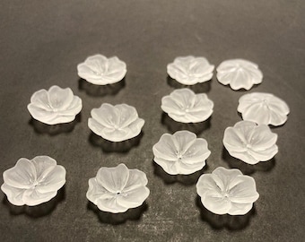 May include: A collection of 11 clear glass flower-shaped embellishments. The embellishments are all the same size and shape, and they have a frosted finish.