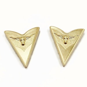 Puede incluir: Un par de puntas de bota vaquera de metal dorado con un diseño de cabeza de toro en relieve.