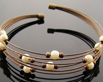 May include: A multi-strand bracelet made of brown wire with white pearl beads. The bracelet is open and has a simple design.