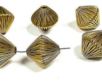 May include: Close-up of several gold-colored, geometric beads. The beads have a ridged, diamond-like shape, with a hole running through the center. Some beads are strung on a thin wire. The beads are set against a white background.