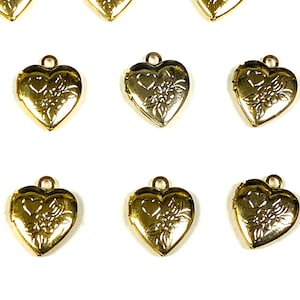 May include: A collection of gold-toned heart-shaped lockets arranged in a grid pattern. Each locket features a small circular bail at the top and an embossed floral design on the front surface, with a smooth, polished metallic finish throughout.