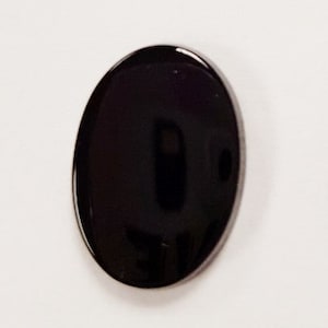 May include: Three black oval-shaped cabochons, one is smaller than the other two. The cabochons are smooth and shiny. A penny is included for size comparison.