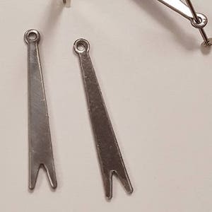 May include: Four silver watch hands, two with forked ends and one with a small hole at the end. The hands are on a white surface.