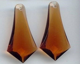 May include: Four amber-colored, teardrop-shaped glass pendants. Each pendant has a pointed bottom and a rounded top with a small hole. The glass has a faceted appearance, catching the light and creating a sparkling effect.