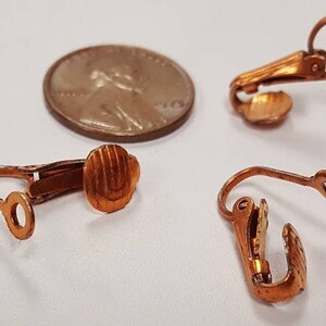 May include: Five copper-toned earring clips. The clips are designed to hold earrings in place. The clips are made of metal and have a smooth finish.