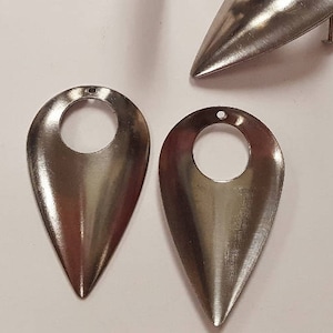 May include: Four silver metal teardrop-shaped earring blanks with a round hole in the center. The blanks are approximately the size of a US penny.