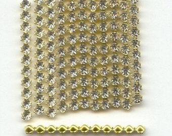 May include: A sheet of clear rhinestone chain trim with a gold metal backing. The chain is made up of small, round rhinestones that are arranged in a grid pattern. A separate gold metal chain trim is also included.