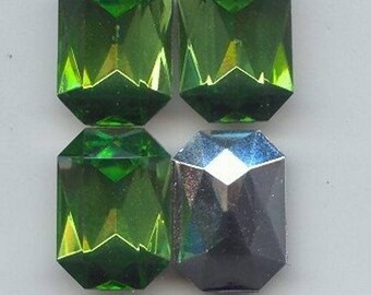 May include: Four emerald green faceted glass gems and one dark gray faceted glass gem. The gems are rectangular in shape and have a shiny finish.