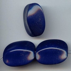 May include: Three blue glass oval beads with iridescent highlights. The beads are smooth and have a slightly rounded shape.