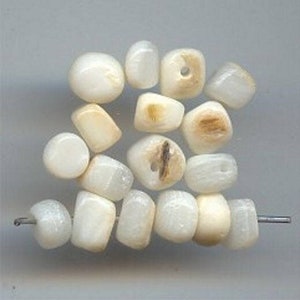 May include: A collection of white and cream colored shell beads. The beads are various shapes and sizes, some are round, some are square, and some are irregular.