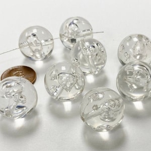 May include: Eight clear glass beads with a textured, bubble-like design. The beads are round and have a hole through the center for stringing.