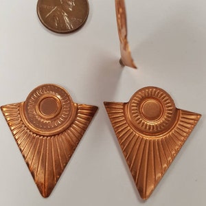 May include: Two copper triangle-shaped earrings with a sunburst design and a circular center piece.