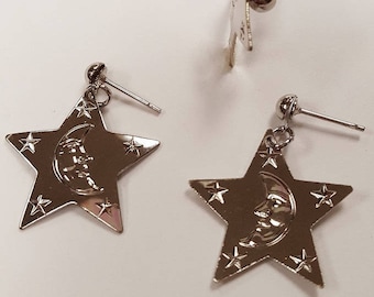 May include: A pair of silver earrings with a crescent moon and star design. Each earring features a five-pointed star with a crescent moon in the center. The stars are surrounded by smaller stars.