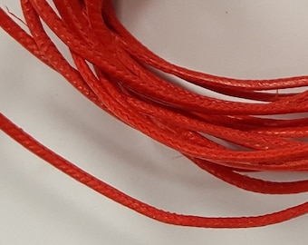 May include: A close-up of a spool of bright red waxed cord. The cord is tightly wound and has a smooth, polished finish.