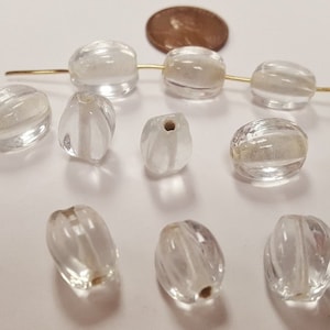 May include: Clear, ribbed glass beads in various sizes and shapes. Some beads are strung on a gold wire, while others are loose. A copper penny is also present, likely for size comparison. The beads have a slightly frosted appearance.