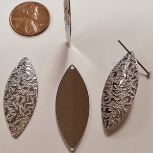 May include: Four silver metal leaf-shaped pendants, two with a textured design and two smooth. The pendants are approximately the size of a US penny.