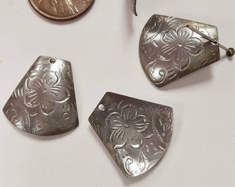 May include: Four silver metal charms with a floral design. The charms are shaped like a curved triangle and have a hole at the top for hanging.