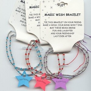 May include: Three friendship bracelets with silver beads and colored string. The bracelets are labeled "Aqua=Happiness", "Red=Power", and "Purple=Luck". The packaging includes the text "Magic Wish Bracelet" and instructions to tie the bracelet on a friend and make a wish.