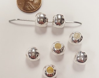 May include: Six silver-toned round beads with a hole in the center. The beads are about the size of a US penny.