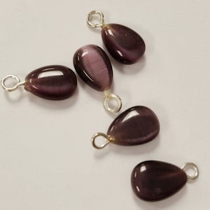 May include: Five purple teardrop-shaped gemstone pendants with silver jump rings. The gemstones have a shimmery, iridescent finish.