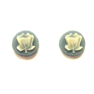 May include: Two small, round earrings with a floral design. Each earring features a light yellow flower on a gray-blue background. The earrings are set against a white backdrop.