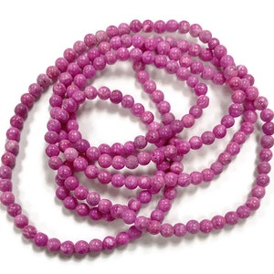 May include: A strand of pink gemstone beads. The beads are round and have a speckled texture.