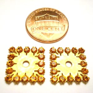 May include: Two square, gold-toned metal components with amber-colored rhinestones around the edges. A U.S. penny is next to the components for size comparison. The components have a hole in the center.