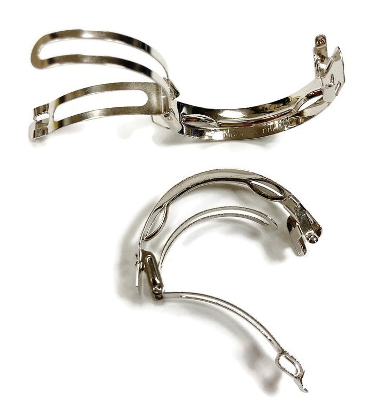 May include: Two silver hair clips with a curved design. The clips are made of metal and have a smooth finish.