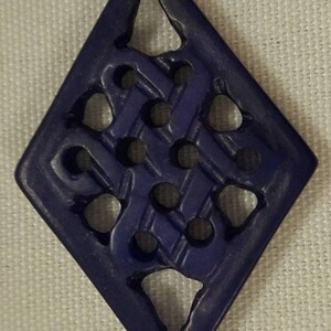 May include: A dark blue diamond-shaped pendant with a carved intricate knot design. The pendant has a smooth, polished finish.