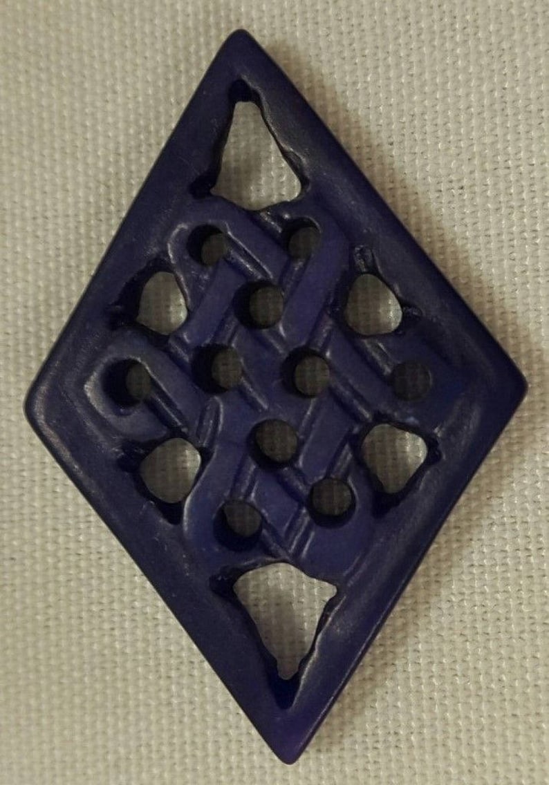 May include: A dark blue diamond-shaped pendant with a carved intricate knot design. The pendant has a smooth, polished finish.
