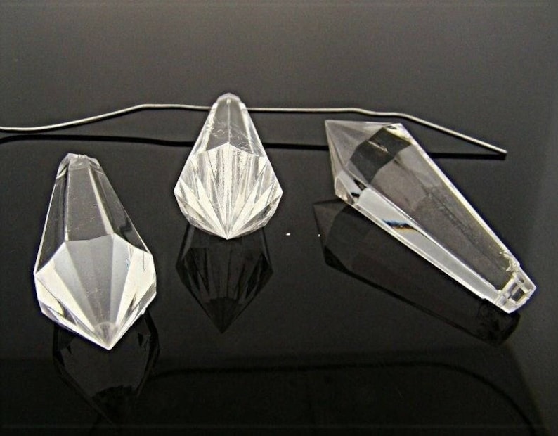 May include: Three clear glass crystal teardrop shapes with a pointed tip. The crystals are hanging from a thin wire.