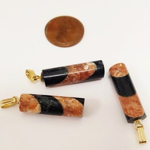 May include: Three gold-toned pendant charms with a black and brown marbled design. The charms are cylindrical in shape and have a loop at the top for attaching to a necklace or bracelet.