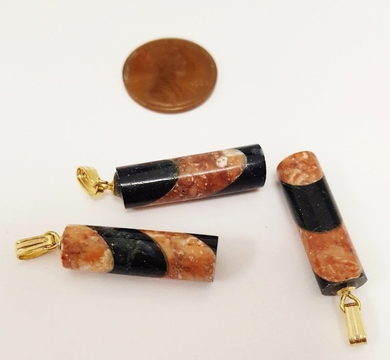 May include: Three gold-toned pendant charms with a black and brown marbled design. The charms are cylindrical in shape and have a loop at the top for attaching to a necklace or bracelet.