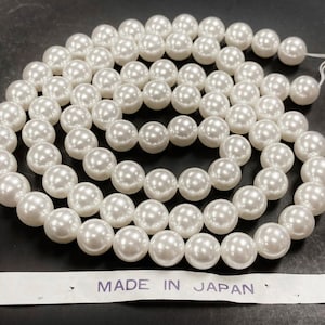 May include: A strand of white faux pearl beads, approximately 10mm in diameter, with a label that reads "MADE IN JAPAN".