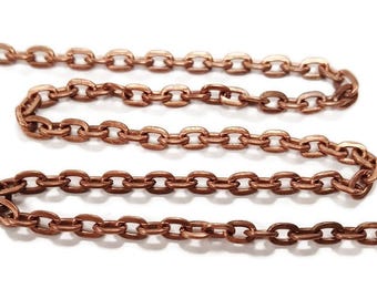 Op de afbeelding: Een close-up van een koperen ketting. De ketting is gemaakt van kleine, ovale schakels. De ketting ligt op een wit oppervlak.