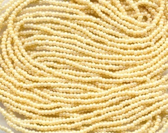 May include: A collection of numerous small, round, cream-colored beads arranged in multiple parallel strands. Each bead features a smooth, opaque finish with a consistent spherical shape, creating a dense, uniform texture across the entire display.