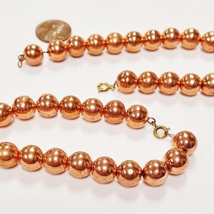 May include: A copper bead necklace with a shiny, metallic finish. The necklace is made of round beads and has a simple design.