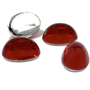 May include: Four red glass cabochons, each with a rounded, slightly domed shape. The cabochons are smooth and glossy, reflecting light.