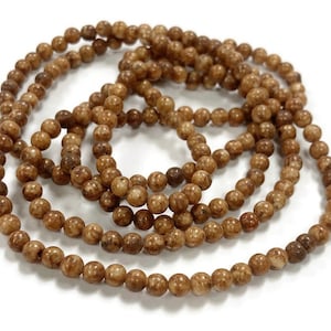 May include: A strand of brown and white speckled round beads. The beads are strung on a clear thread and are approximately 6mm in diameter.