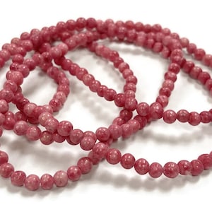 May include: A strand of pink gemstone beads. The beads are round and have a speckled texture.