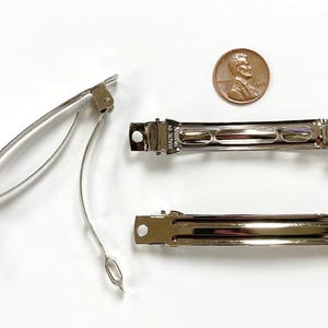 May include: Three silver metal hair clips. The clips are about 2 inches long and have a smooth, shiny finish. The clips are designed to hold hair in place.