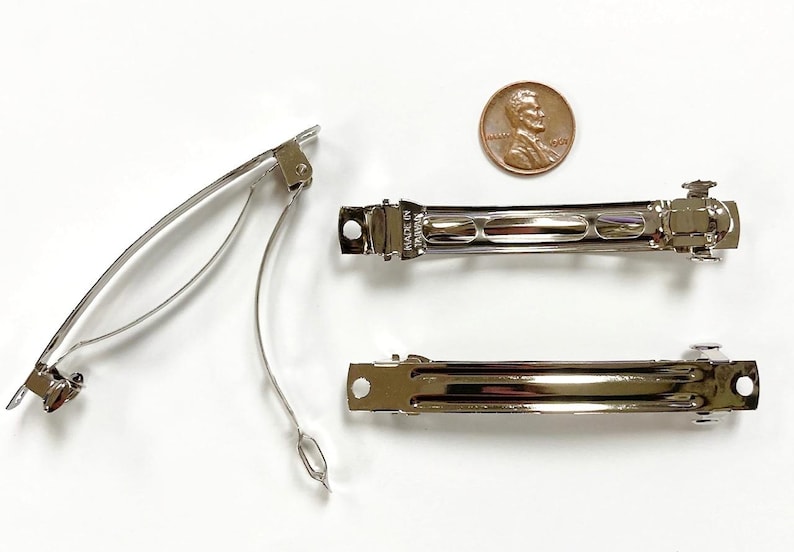 May include: Three silver metal hair clips. The clips are about 2 inches long and have a smooth, shiny finish. The clips are designed to hold hair in place.